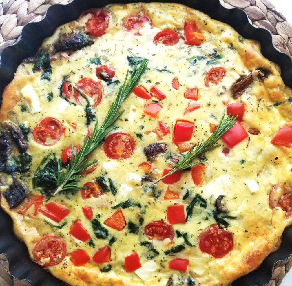 Frisch gebackene Low-Carb-Quiche mit Spinat, Paprika, Champignons und Feta auf rustikalem Holztisch.